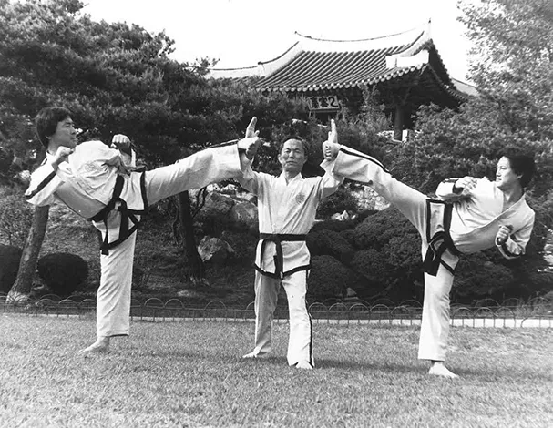 Photographie d'époque montrant 2 pratiquants de Taekwondo effectuant un coup de pied latéral bloqués par un troisième personnage central